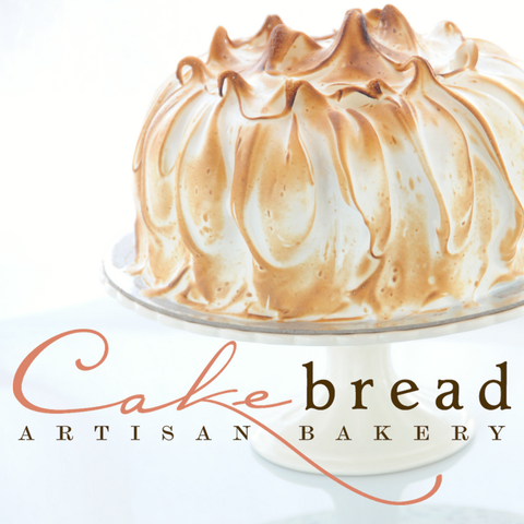 A delicious looking cake covered in toasted meringue on a cake stand with the logo of Cakebread Artisan Bakery in front.