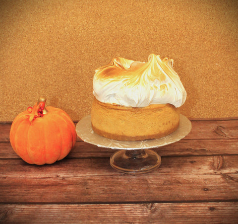 A New York-Style Pumpkin Spice Cheesecake with a meringue topping, displayed on a wooden surface next to a pumpkin.