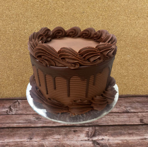 A round chocolate lovers dream cake with piped frosting rosettes on top and around the base, set on a silver cake board against a gold glitter backdrop and rustic wooden surface.