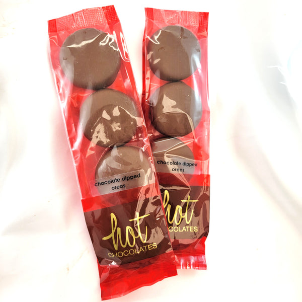 Two packs of chocolate dipped oreo cookies on a white background. The packaging is red and clear, showing the chocolate-covered cookies inside, with 'hot chocolates' written in gold on the lower section.