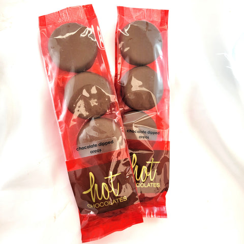 Two packs of chocolate dipped oreo cookies on a white background. The packaging is red and clear, showing the chocolate-covered cookies inside, with 'hot chocolates' written in gold on the lower section.