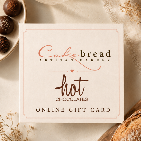 A square gift card from Cakebread Artisan Bakery and Hot Chocolates, styled in a flat lay with chocolate pieces, bread, and dried flowers on a neutral beige background.