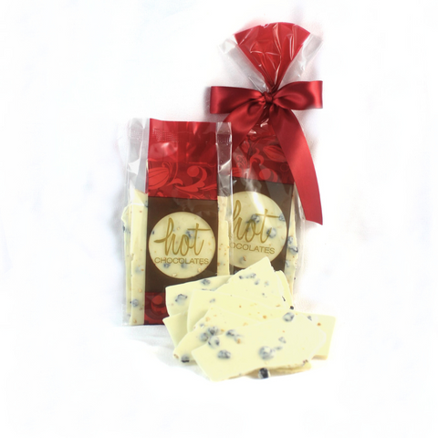 2 bags in red and brown with a red bow filled with artisan lemon blueberry chocolate bark in white chocolate, with an example in front.
