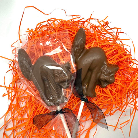 2 milk chocolate Spooky Chocolate Cat Lollipop Suckers shown with an arched back and hissing mouth, placed on a white surface surrounded by orange shred.