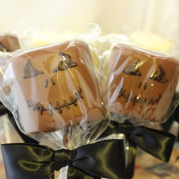 2 Chocolate Dipped Marshmallow Goblin Pops, shown in milk chocolate with dark chocolate creepy faces, packaged with clear bags and black bows.