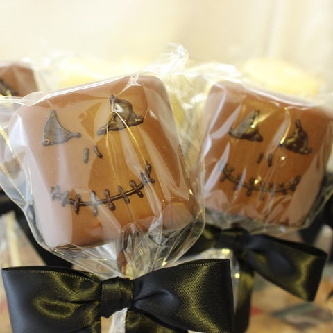 2 Chocolate Dipped Marshmallow Goblin Pops, shown in milk chocolate with dark chocolate creepy faces, packaged with clear bags and black bows.