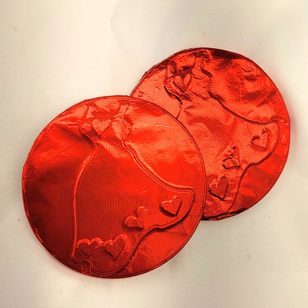 Two medallion red foil-wrapped chocolates with embossed Red Dress designs, photographed on a plain off-white background.