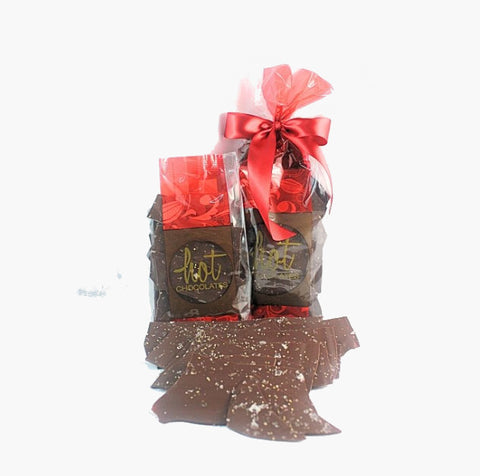 A packaged gift set of artisan chocolate salt & pepper bark in thin dark chocolate shards, presented with a red ribbon.