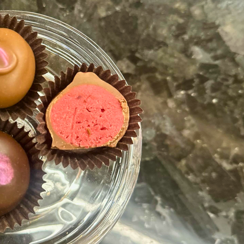 Close-up of pink and brown hand dipped sakura chocolate truffles on silver tray on a marble surface.