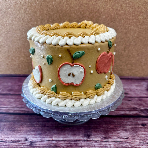 A fun no gluten added cake with caramel colored dairy-free frosting and a red apple design along the sides.