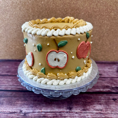 A fun no gluten added cake with caramel colored dairy-free frosting and a red apple design along the sides.