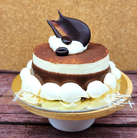 A chocolate and cream layered no gluten added Italian cake with piped meringue decorations on the sides, topped with chocolate and coffee beans, displayed on a gold cake stand.