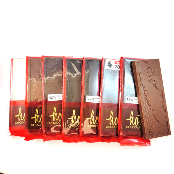 Seven bars of chocolate in red wrappers arranged in a row on a white background, with one bar standing upright on the right showing a detailed Van Isle map design. The wrappers display the brand 'hot CHOCOLATE' and various chocolate percentages.