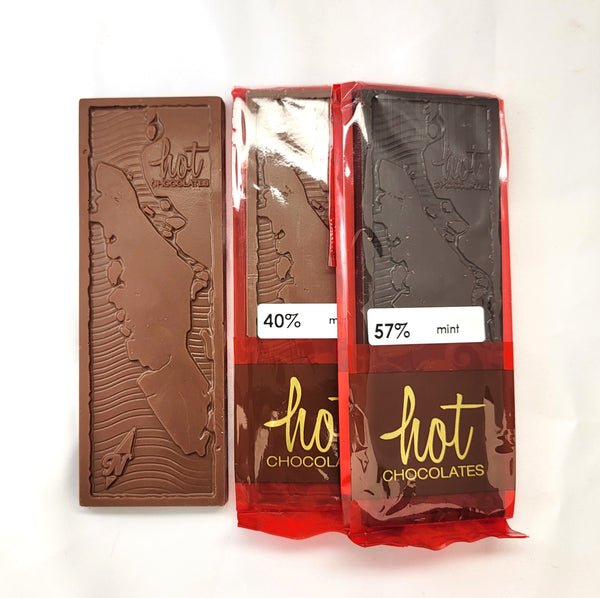 Three chocolate bars from hot chocolates, one unwrapped showing an artisan milk chocolate bar with embossed Vancouver Island map, and two wrapped in red packaging showing dark chocolate bars labeled 40% and 57% mint.