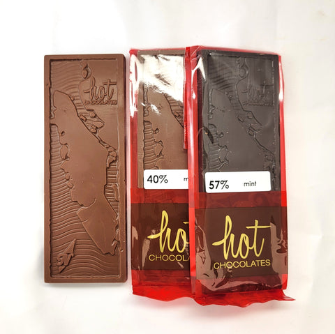 Three chocolate bars from hot chocolates, one unwrapped showing an artisan milk chocolate bar with embossed Vancouver Island map, and two wrapped in red packaging showing dark chocolate bars labeled 40% and 57% mint.