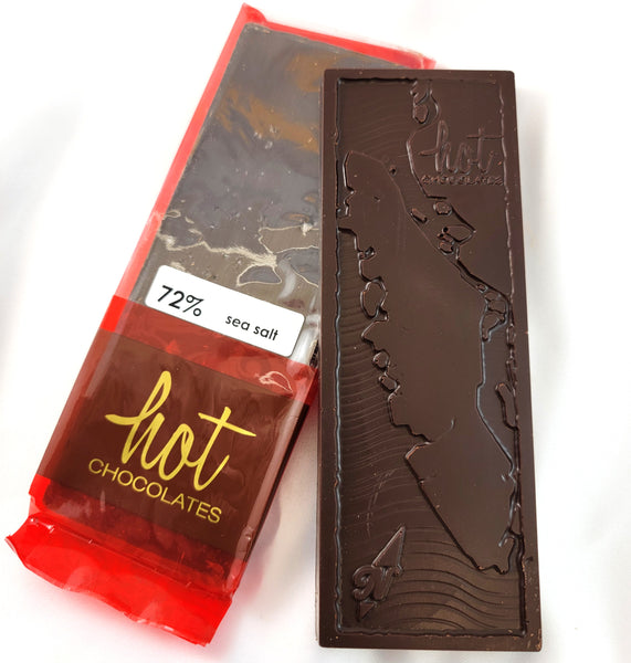 A dark chocolate bar with an embossed Vancouver Island map design, shown next to its red wrapper labeled '72% sea salt' and 'hot CHOCOLATES' on a white background.