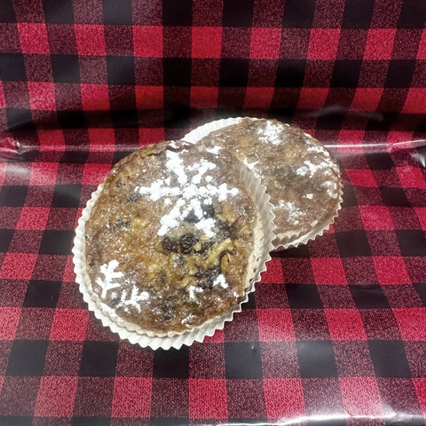 Two Canadian artisan butter tarts with powered sugar snow flake designs on the top, shown on a rustic background of buffalo plaid.