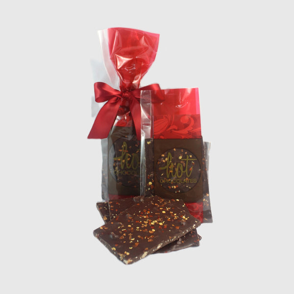 Packaged artisan dark chocolate chili bark with almond toffee and chili flakes, presented in a clear plastic bag with a red ribbon.