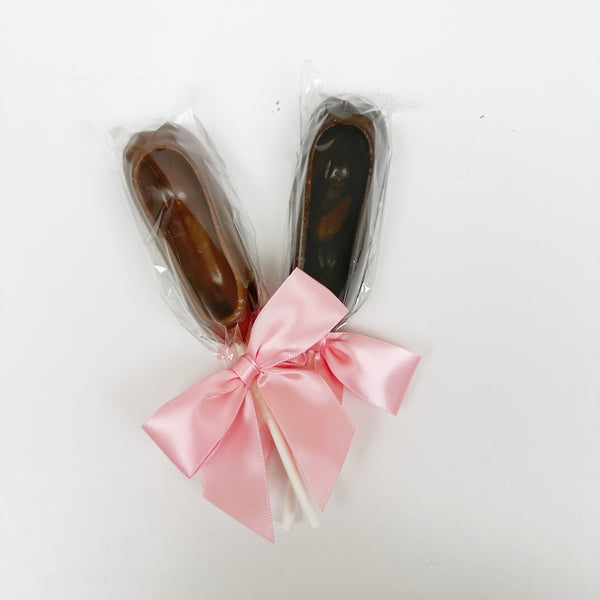 Two chocolate ballet slipper suckers, wrapped in clear packaging with pink bows.