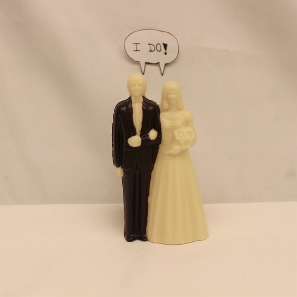 An image of a chocolate wedding cake topper bride and groom, with a thought bubble above, reading 'I do!'.