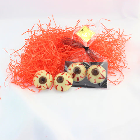 A photo showing two sets of Creepy Bloodshot Chocolate Eye Balls with a clear packaging bag, all placed on a white surface with orange shred around.