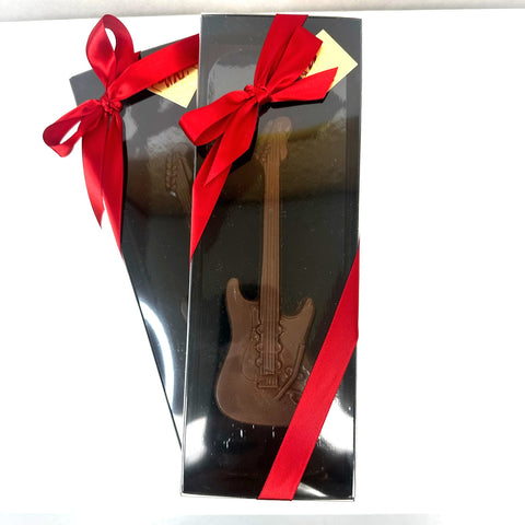 A gift boxed Strats-style solid chocolate electric guitar model, packaged in a box with a red ribbon on top.