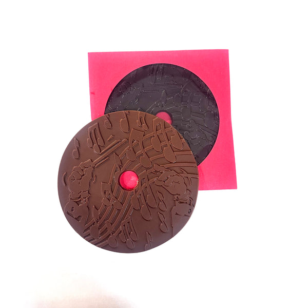 An artisan Chocolate record with musical notes designed on it, shown in milk and dark on a white background, with one in a red record sleeve.