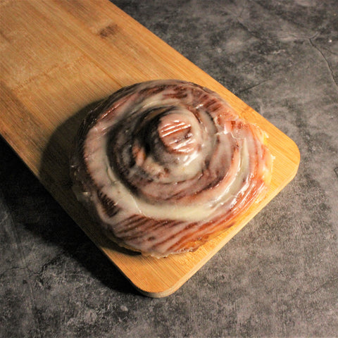 A cinnamon frosted artisan cinnamon roll on a wooden board.