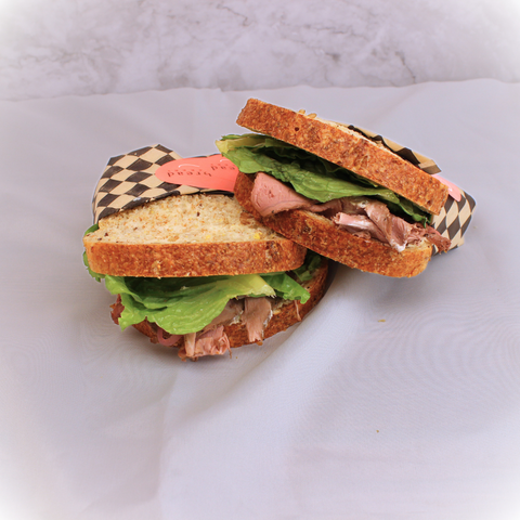 2 house-made corned beef on rye sandwiches wrapped in bakers paper, with a pink logo, on a white background.