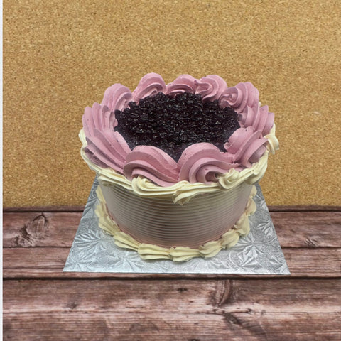 A wild blueberry and earl grey layer cake with purple and beige frosting on a wooden surface.