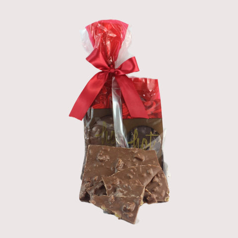 2 red and brown bags with a red bow and an example of artisan chocolate ginger bark in the forefront, with visible chunks of stem ginger in the chocolate.