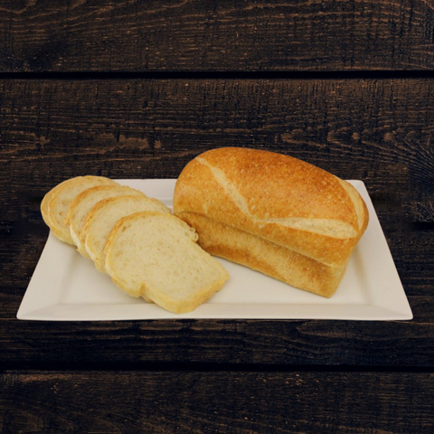 A loaf of  whole wheat sourdough sandwich bread with some slices cut, placed on a white plate on a wooden surface.