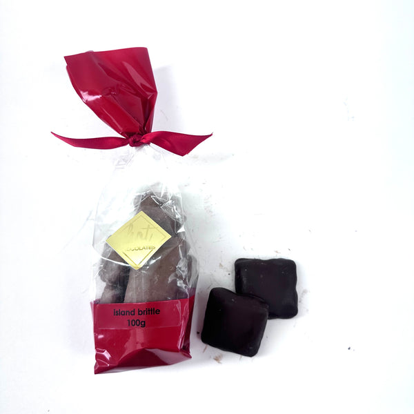 Packaged Artisan chocolate covered almond toffee called Island Brittle with a red label and bow on a white background