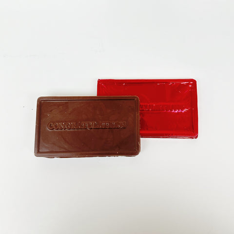Two Oat Milk Chocolate Congratulations Bars, one with  red foill, one lying horizontally and the other standing upright, both with 'CONGRATULATIONS' text on the front.