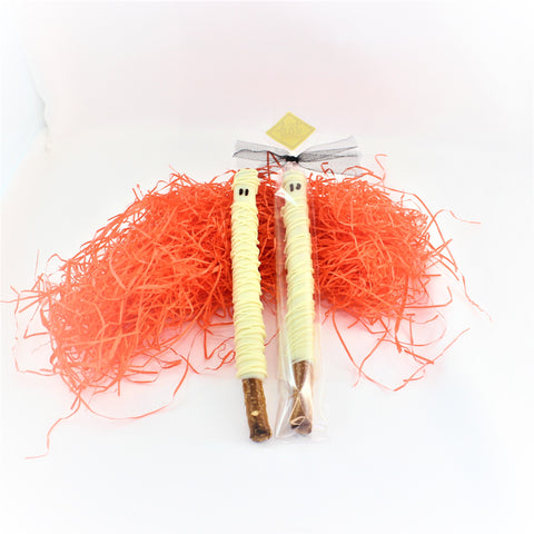 2 Chocolate Dipped Pretzel Mummy Treats laying on a bed of white shred, packaged in a clear bag, tied with a black tie. 