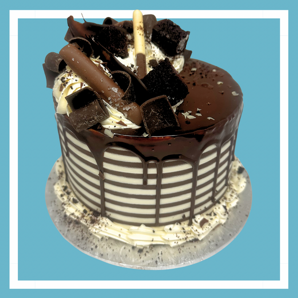 A gourmet vanilla chocolate tuxedo cake with stripped sides and piled high with chocolate decorations on a blue background.