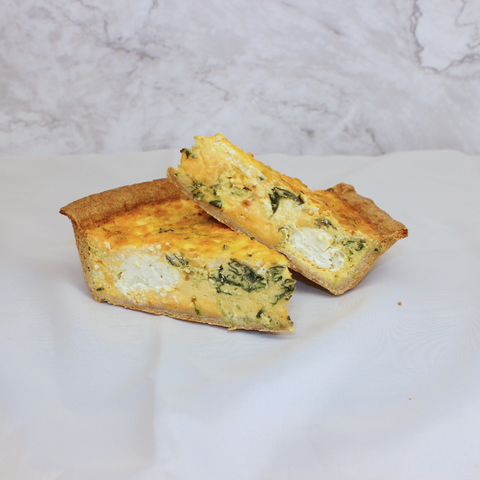2 house-made vegetarian quiche slices showing the cheesy and vegetable filled interior of the flaky crust on a white background.