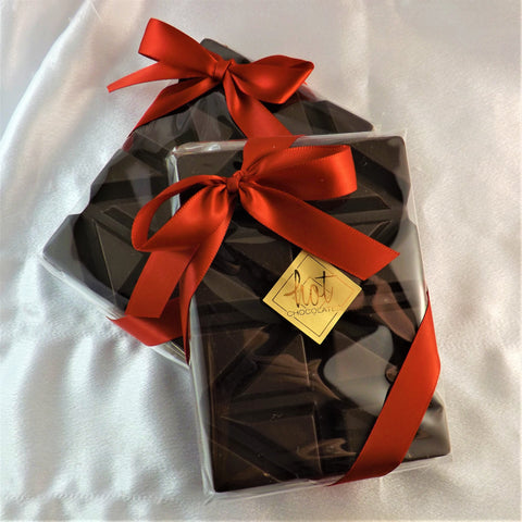 A single origin chocolate bar made from 100% Colombian chocolate with a red ribbon and a gold-colored label, placed on a white surface.