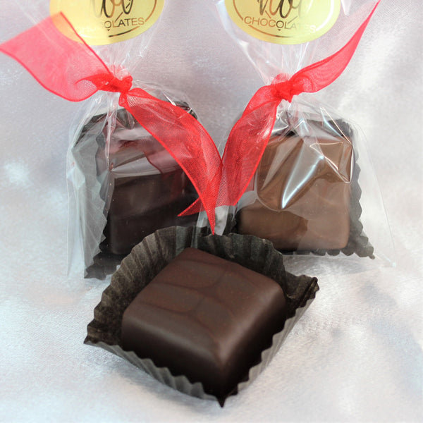 An artisan chocolate B52 Square in front with 2 more packaged with red ribbons on a white surface.