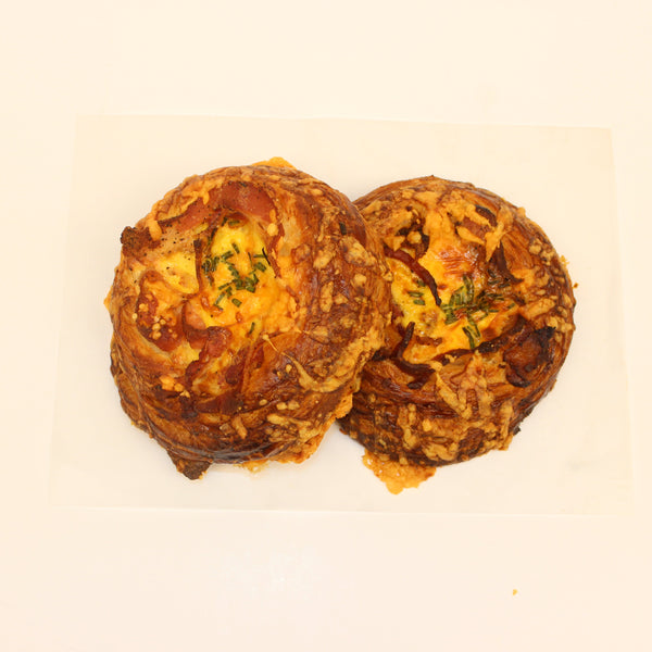 Two golden brown artisan croissant breakfast sandwiches with visible toppings of egg, bacon, and cheese on a white plate.