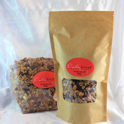 Two packages of Cakebread Artisan Bakery granola, one transparent and one with a beige wrapper, showcasing a mix of seeds, nuts, and dried fruits.