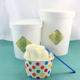 A cup of Comox Valley Artisan gelato with a colorful polka dot pattern next to two larger containers of gelato in white tubs with gold labels.