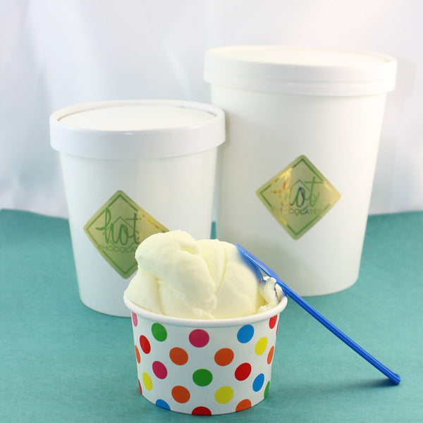 A cup of Comox Valley Artisan gelato with a colorful polka dot pattern next to two larger containers of gelato in white tubs with gold labels.