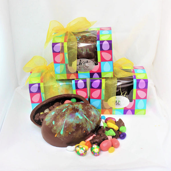 A 3d candy-filled chocolate Easter egg with a collection of chocolate eggs with decorative and assorted candies, presented in a bowed box with yellow ribbon bows on top.