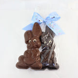 Solid chocolate Easter Bunny named Cuddly, shown in dark and milk chocolate, one packaged in clear with a blue bow.