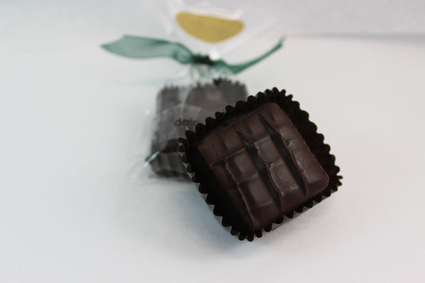 A mint dairy free chocolate square, packaged with a green bow and another in front without packaging on a white background.