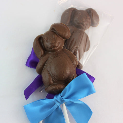 A picture of 2 chocolate Easter Bunny suckers with a  blue bow on one and a purple bow on the other.