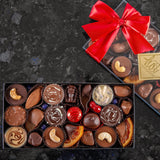 A large artisan chocolate fruit & nuts gift box, filled with chocolate covered treats with a red ribbon on top.