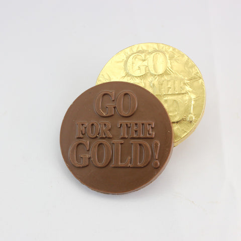 A chocolate coin with the phrase 'GO FOR THE GOLD!' embossed on it, placed next to a gold-foiled coin with the same embossing.