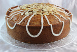 A delicious classic lemon almond pound cake, topped with icing drizzle and toasted almonds on a silver disk and a white background.